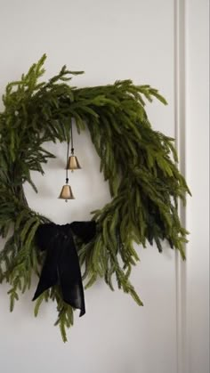 a wreath with bells hanging from it's side on a door handle and decorated with evergreen leaves