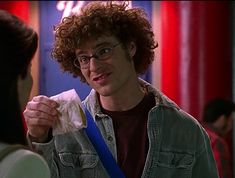 a man with curly hair and glasses is holding something in his hand while talking to another person