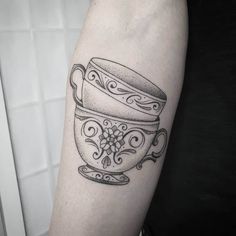 a black and white photo of a teacup tattoo on the right arm with an ornate design