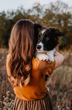 a woman holding a black and white dog in her arms while standing in a field