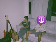 two people sitting on a couch with guitars and peace sign in the corner behind them