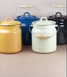 four different colored pots with handles and lids on the top one has a wooden stick sticking out of it