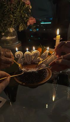 two people are lighting candles on a cake with the number twenty nine on it, while another person is holding a lit candle in front of them