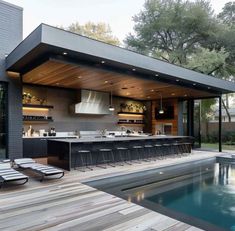 an outdoor kitchen next to a pool in the middle of a yard with lounge chairs