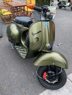 a green scooter parked on the side of a street next to tables and chairs