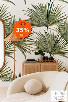 a white couch sitting under a palm tree next to a wall with an orange sale sign