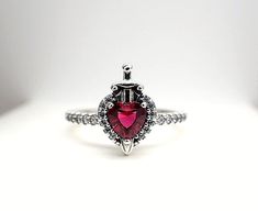 a ring with a heart shaped red stone in the center