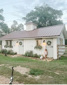 a woman standing in front of a small white house with a metal roof and door