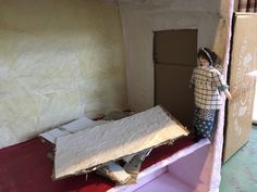 a doll is standing next to a bed in a room with cardboard on the floor