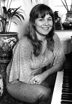 a woman sitting at a piano in front of a potted plant and smiling for the camera