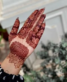 a woman's hand with henna on it and some plants in the background