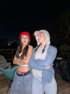 two young women standing next to each other on a wooden deck at night with their arms crossed