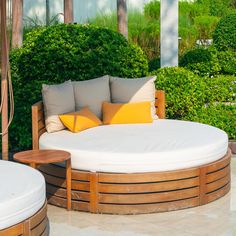 an outdoor seating area with round wooden benches and pillows on the cushions, surrounded by greenery