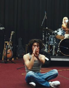 a man sitting on the floor with his hands clasped in front of him and other instruments behind him