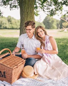 a man and woman sitting under a tree holding drinks