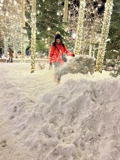 a person in red jacket on snowboard next to trees and christmas lights at night