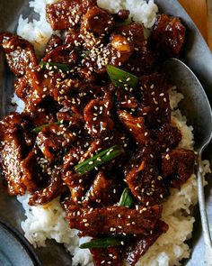 a plate filled with rice and meat on top of a wooden table next to a spoon