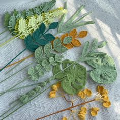 several crocheted leaves and plants on a white tablecloth with green stems, yellow flowers, and other foliage