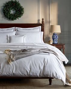 a bed with white sheets and pillows in a bedroom next to a wreath on the wall