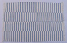 a blue and white striped rug with fringes on it's edges, against a light blue background