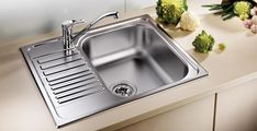 a stainless steel kitchen sink and countertop with flowers on the table in the background