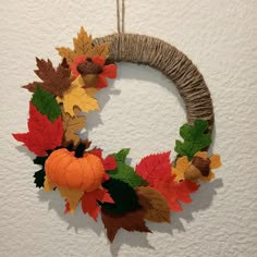 a wreath with leaves and acorns hanging on a wall next to a white wall