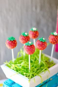 strawberries are on top of green grass in a white bowl with toothpicks