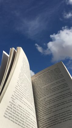 an open book sitting on top of a table under a blue sky with white clouds