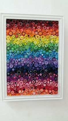 a painting made with buttons on a white frame hanging on the wall in a room