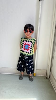 a little boy standing in front of a white wall holding a crocheted object