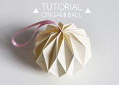 an origami ball with pink ribbon hanging from it's side on a white surface