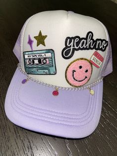 a purple and white hat with an embellished smiley face on the front that says yeah no