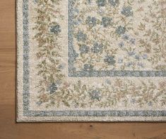 an area rug with blue and green flowers on it, sitting on a wooden floor