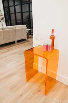 an orange glass side table with two wine glasses on it in front of a white wall