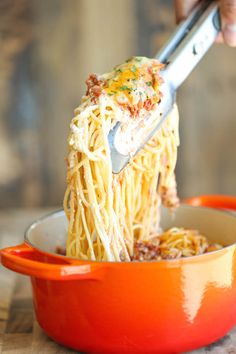 someone is eating spaghetti with a fork in a red bowl on a wooden tablecloth