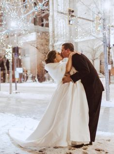 a bride and groom kissing in the snow on their wedding day at city hall park