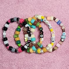 three bracelets with letters and beads on a pink carpeted area, one is for sale