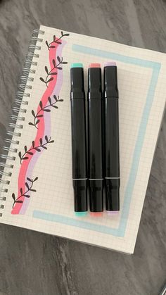 three pens sitting on top of a notebook