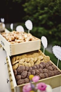 two wooden boxes filled with cookies on top of a table next to flowers and paper signs