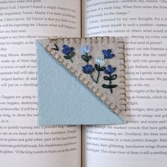 an open book with a piece of felt and embroidered flowers on the front cover, sitting on top of it