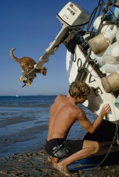 a man and his cat are on the beach by a boat with it's mooring ropes