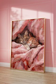 two kittens are laying on a pink blanket in front of a framed art piece