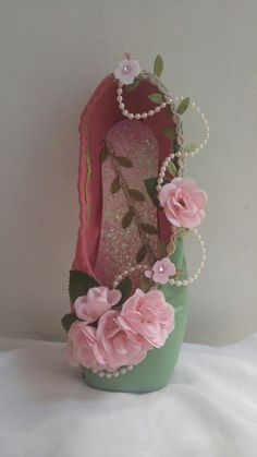 a green vase with pink flowers and pearls on the bottom is sitting on a white surface