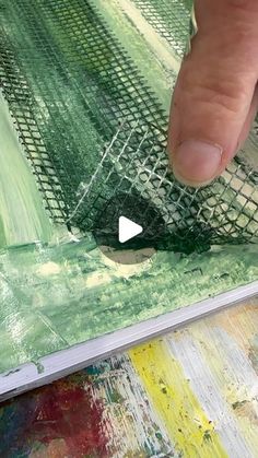 someone is painting with green and yellow colors on the canvas, while another hand points at it