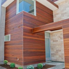 a modern house with wood siding on the side and landscaping around it, including shrubs