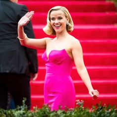 a woman in a pink dress waves to the crowd as she walks up steps with her hand on her hip