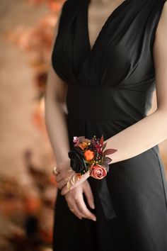 a woman wearing a black dress holding a bouquet of flowers in her left hand and an orange flower on her right wrist