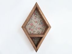 a wooden shelf with floral fabric in the middle on a white wall behind it is an open hexagonal wood frame