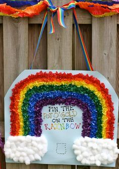 a rainbow sign hanging on the side of a wooden fence with streamers around it