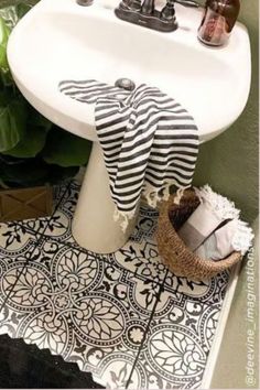 a white sink sitting next to a green plant on top of a black and white floor